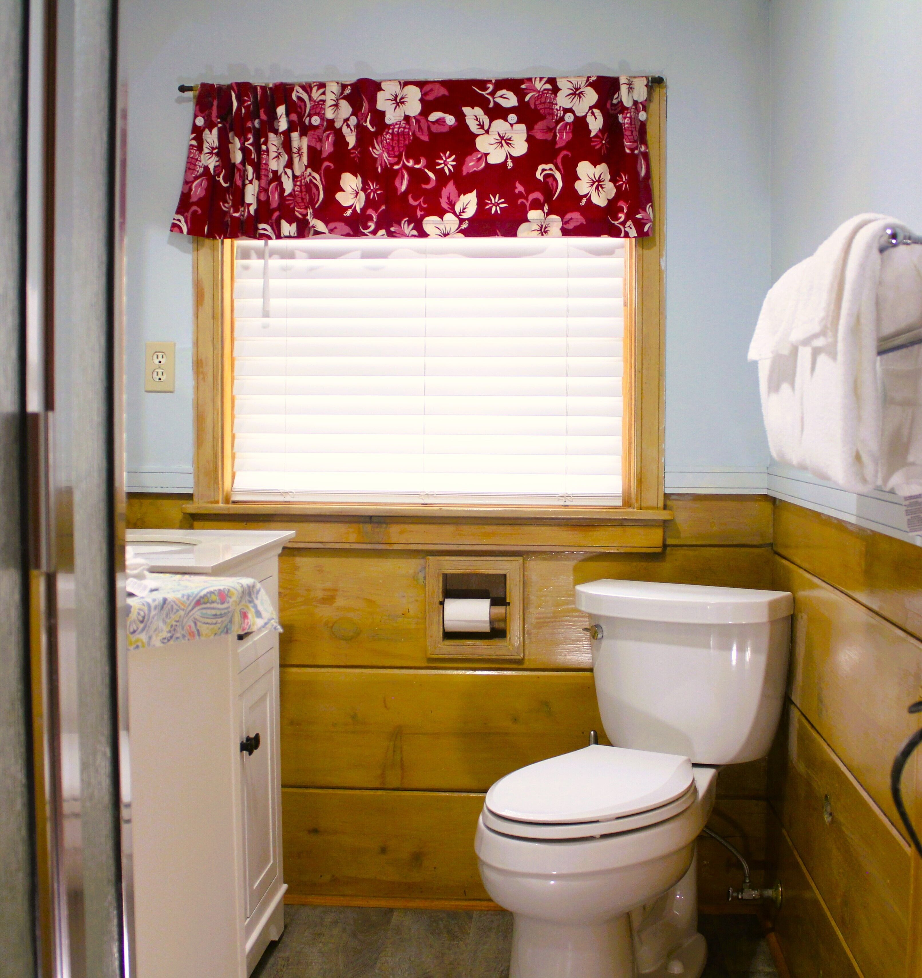 Une salle de bain avec des toilettes, un lavabo et une fenêtre avec des stores.