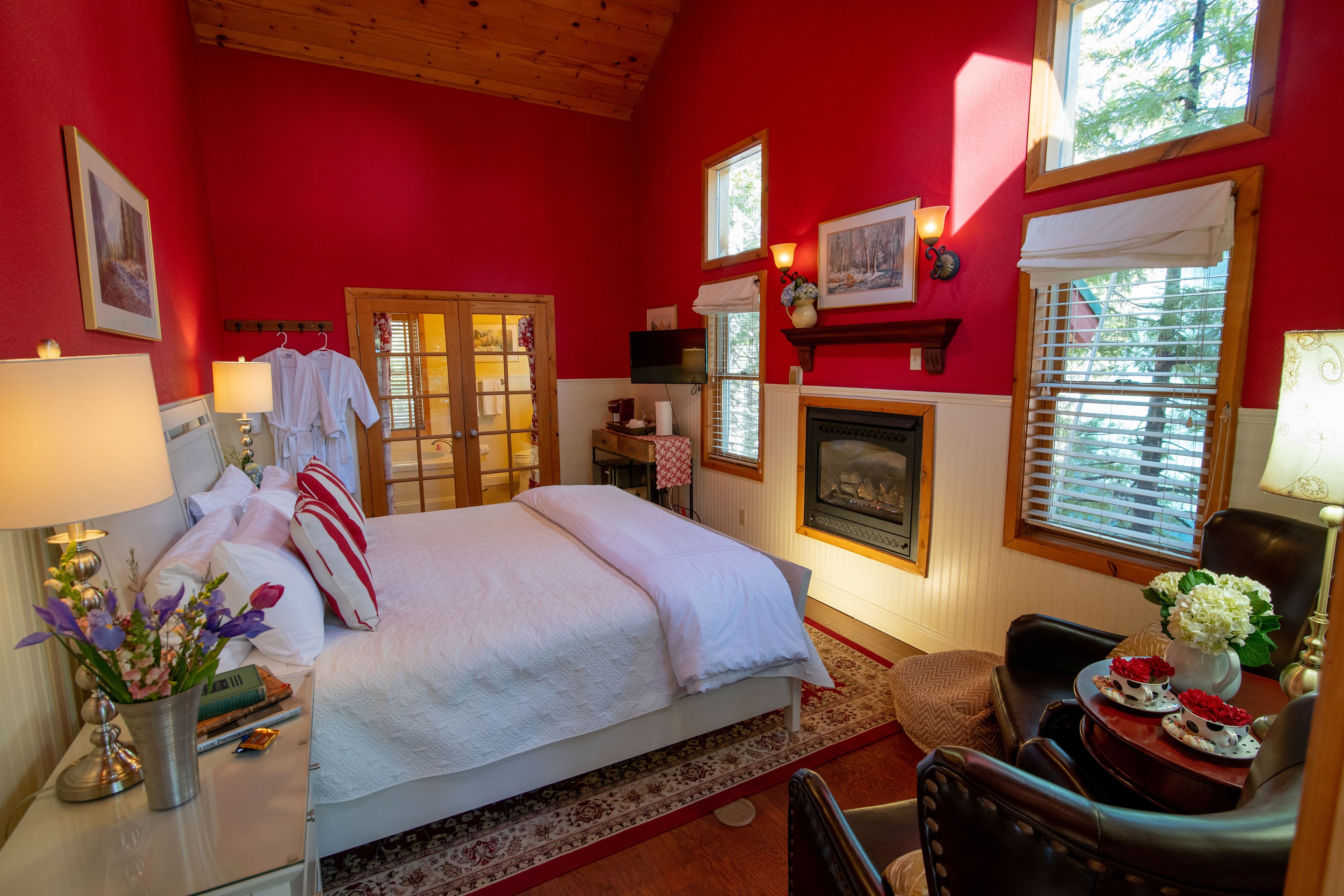 Een slaapkamer met een bed, een stoel, een tafel met een lamp, een open haard en een raam.