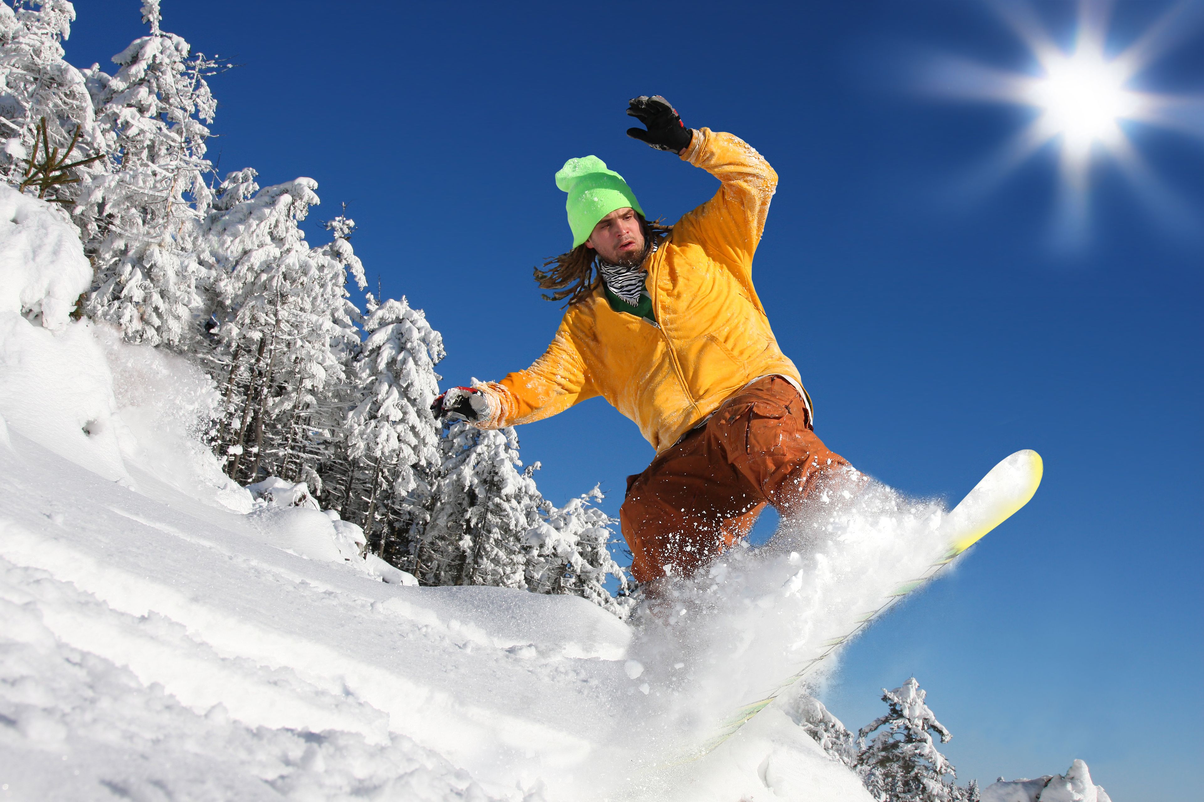 A snowboarder in a yellow jacket and brown pants performing a jump on a snowy slope.