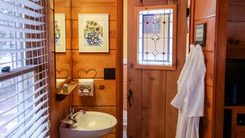 Un baño de madera con un lavamanos blanco, un perchero y una ventana con un diseño de vidrio emplomado.