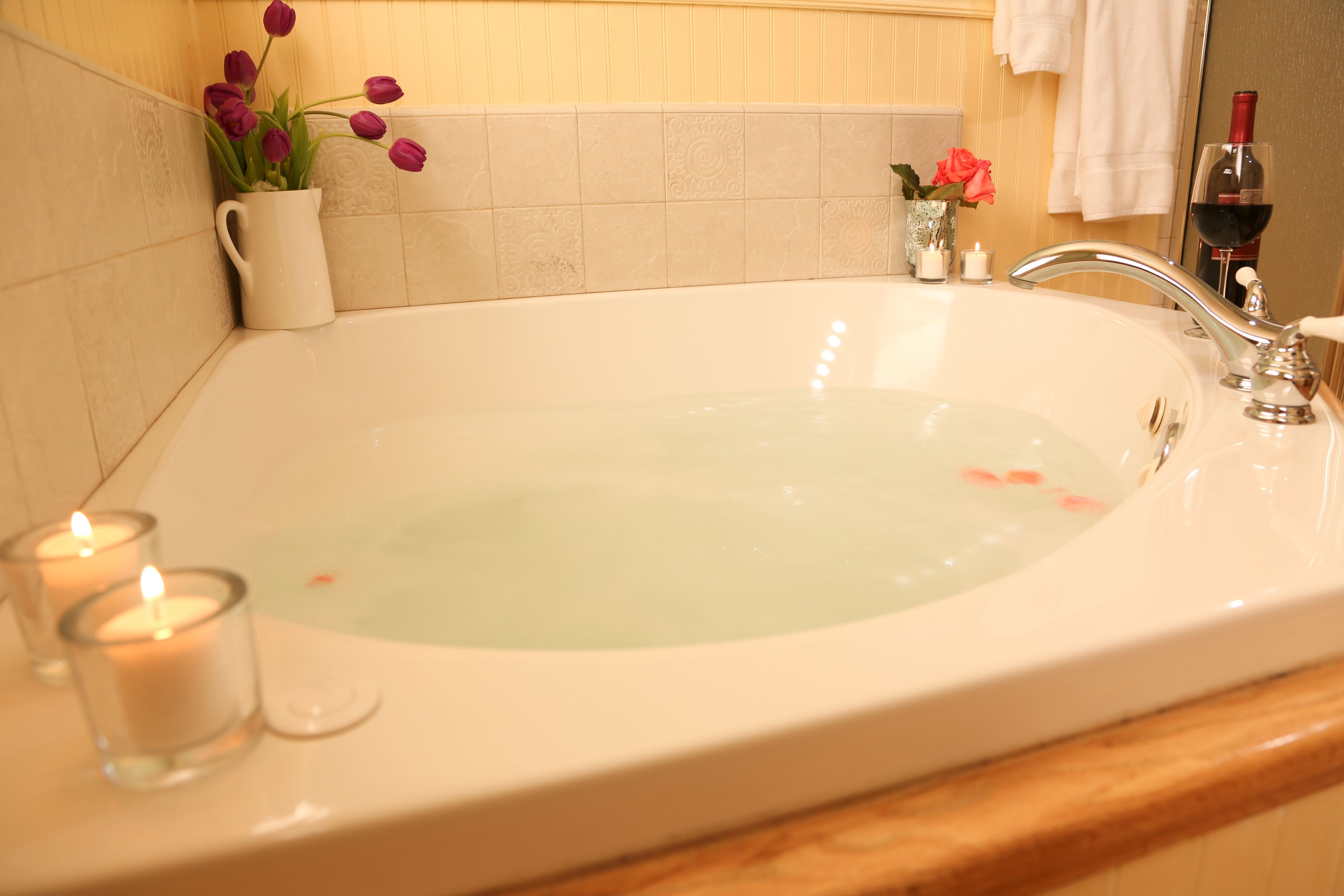 Una bañera con interior blanco, un candelabro de vidrio y un florero con flores.