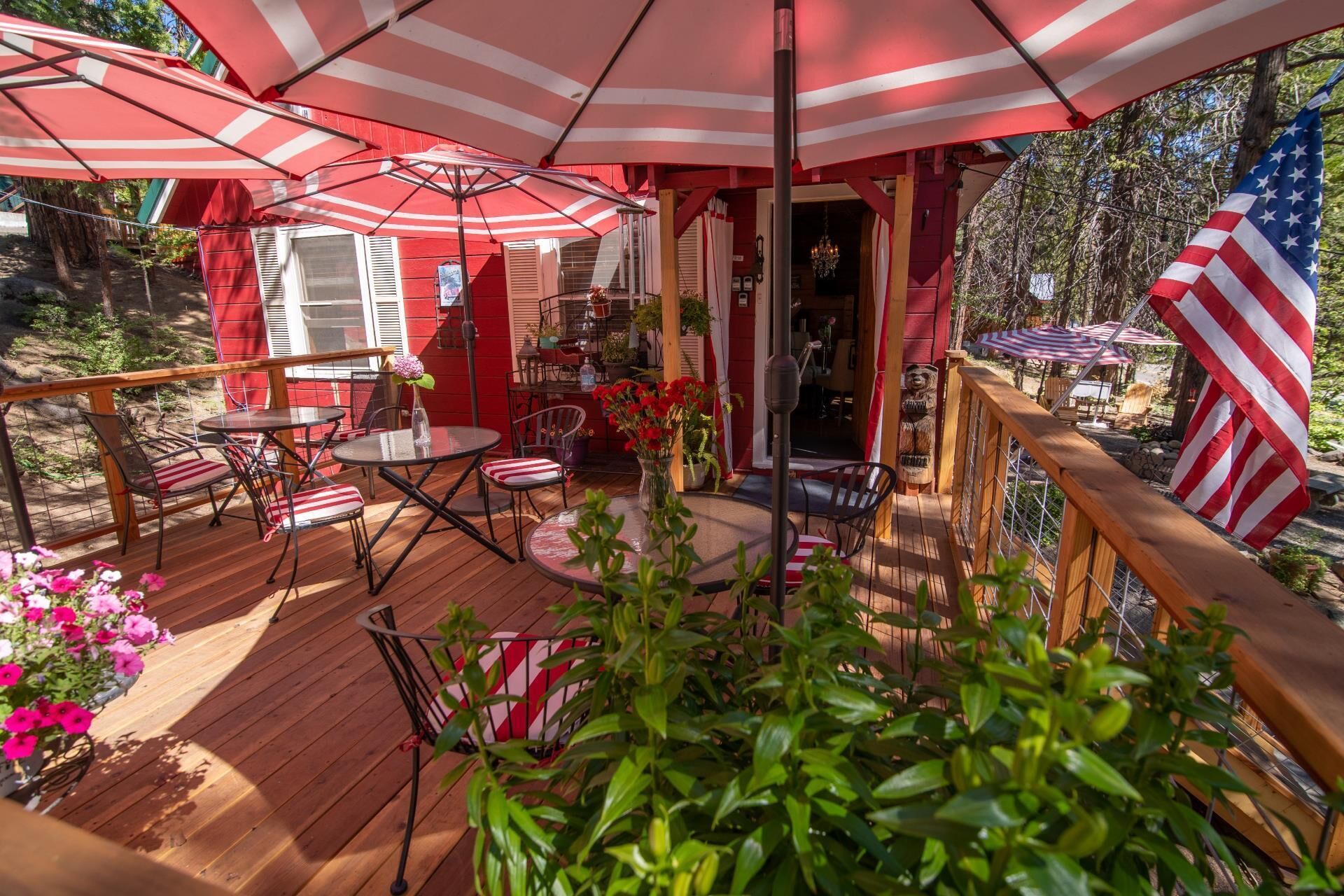 A wooden deck with outdoor seating, including tables and chairs, and a covered area with striped umbrellas.
