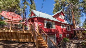 A red wooden house with a green roof, a wooden staircase, and a stone wall.