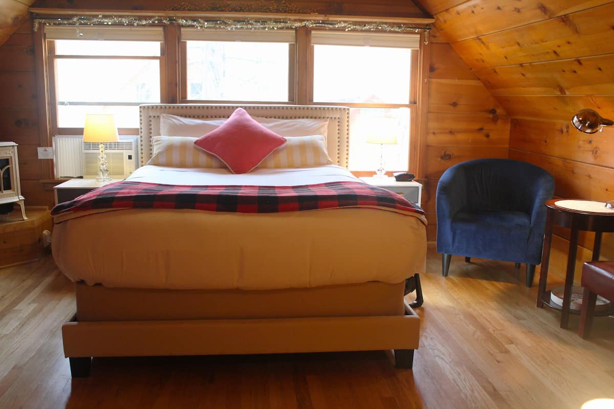 A cozy room with a large bed, a chair, a small table, and a window with curtains.