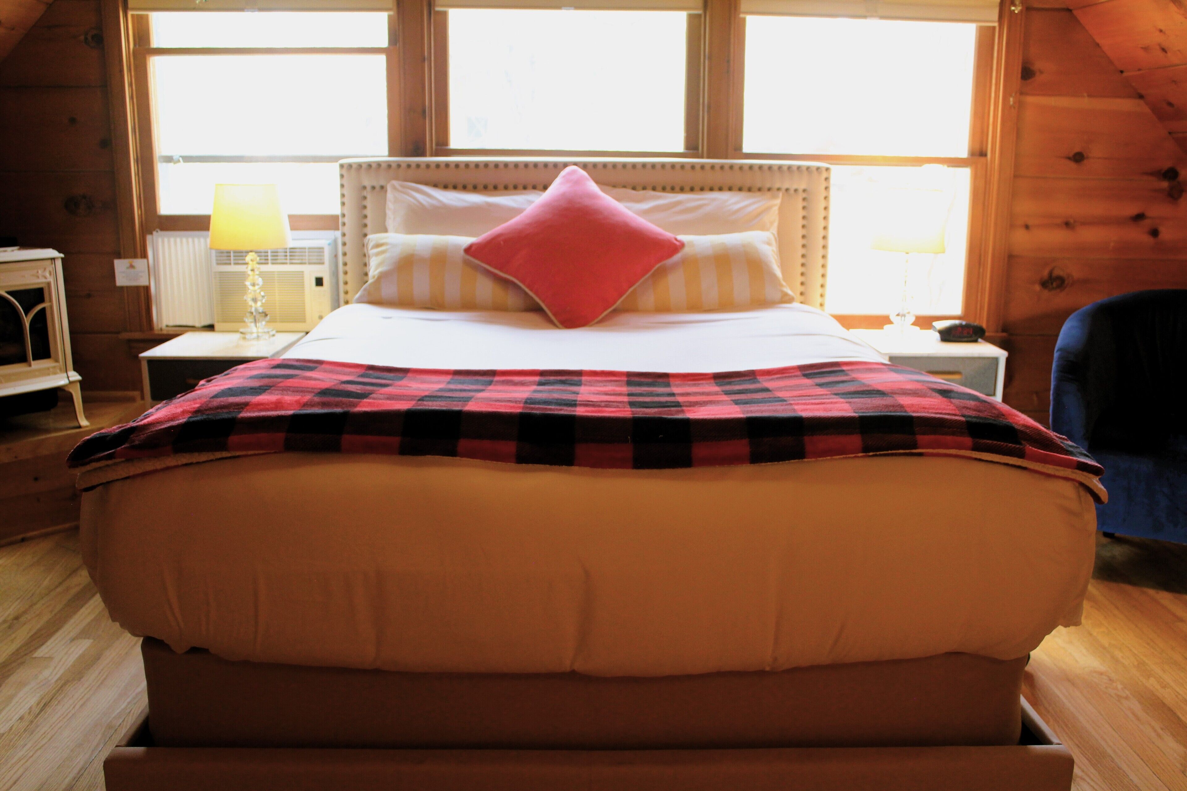 Un dormitorio con una cama grande, un cabecero de madera, un almohadón rojo y una manta a cuadros.