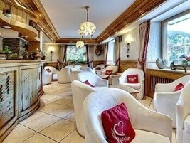 Un intérieur chaleureux avec des boiseries, des fauteuils blancs à revêtement en tissu agrémentés de coussins rouges, un coin bar et de grandes fenêtres offrant une vue sur l’extérieur.