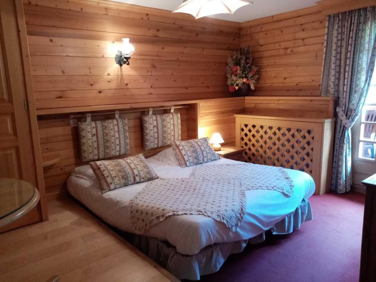 Ein Schlafzimmer mit Holzvertäfelung, einem Bett, einem Nachttisch, einer Lampe und einem Fenster mit Vorhängen.