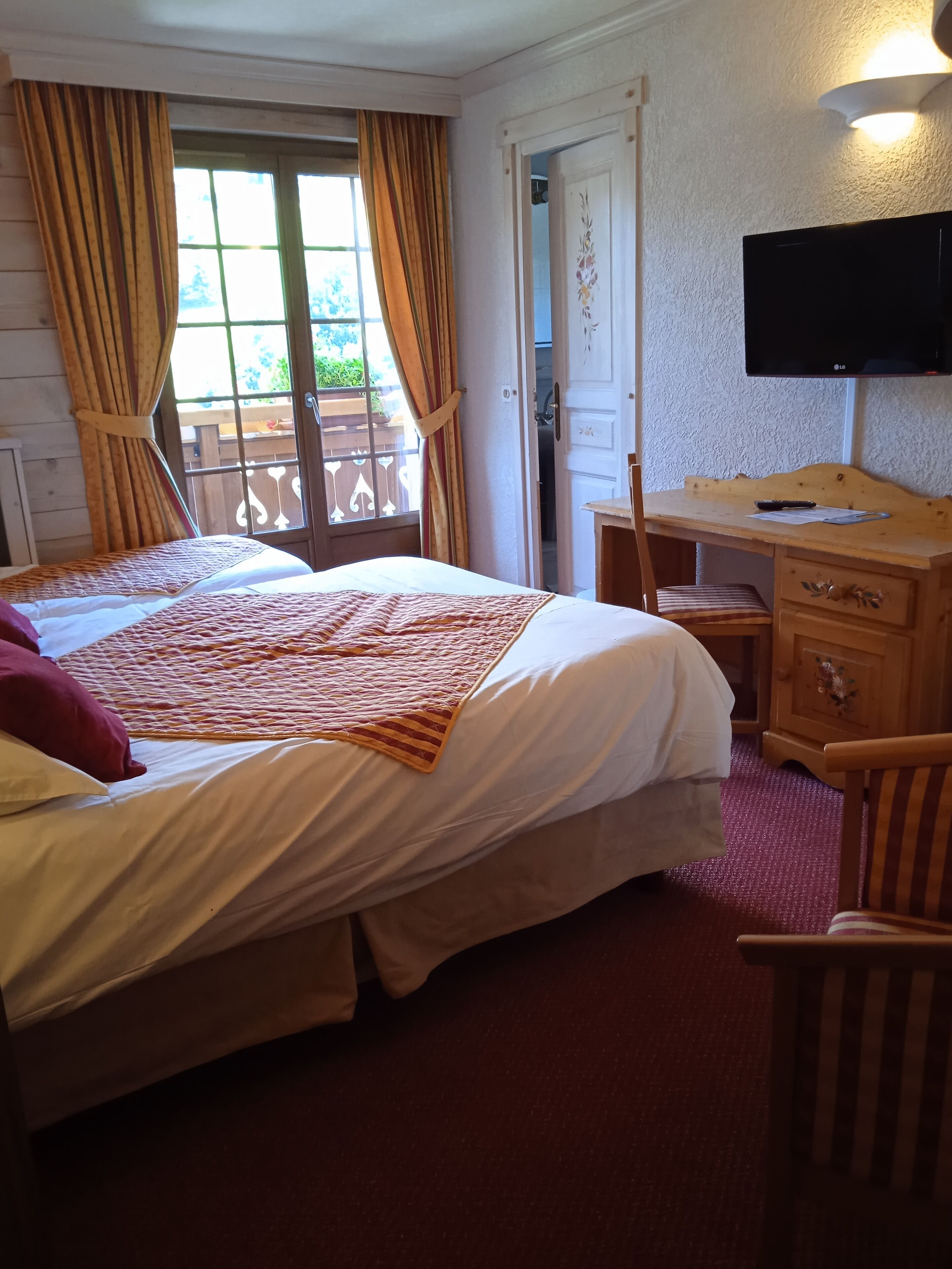 Ein Hotelzimmer mit Bett, Schreibtisch, Stuhl, Fernseher und einem Balkon mit Vorhängen.