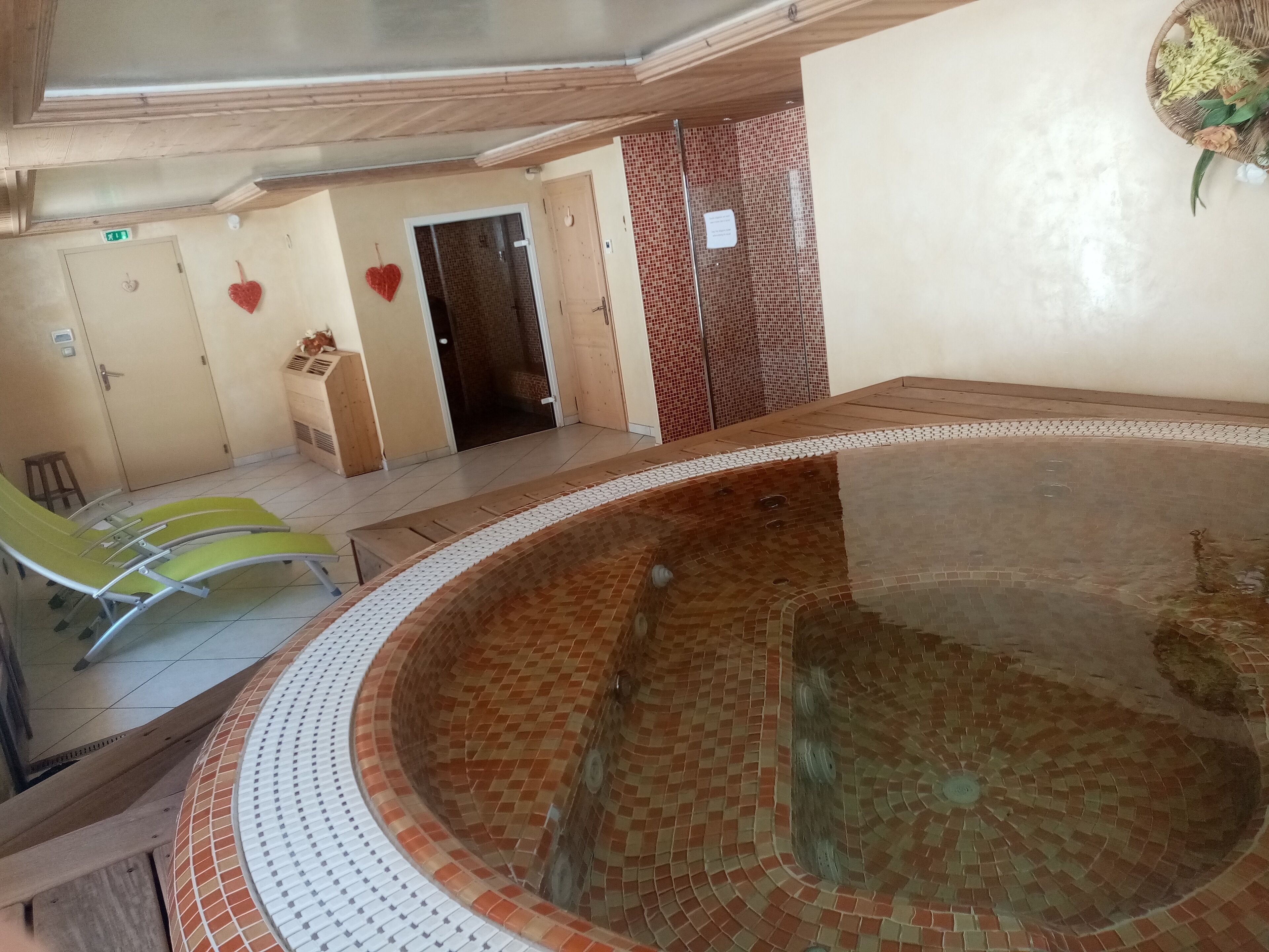 Un espace spa comprenant un bain à remous carrelé, des chaises longues et une porte donnant accès à une salle de douche.