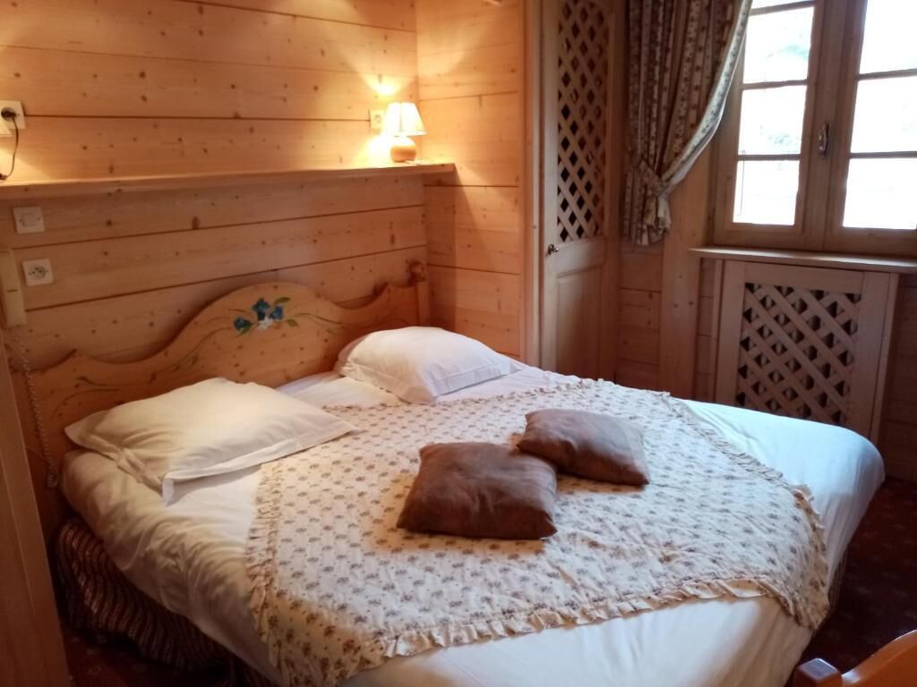 A wooden-paneled room with a bed, a wall-mounted lamp, and a window with curtains.