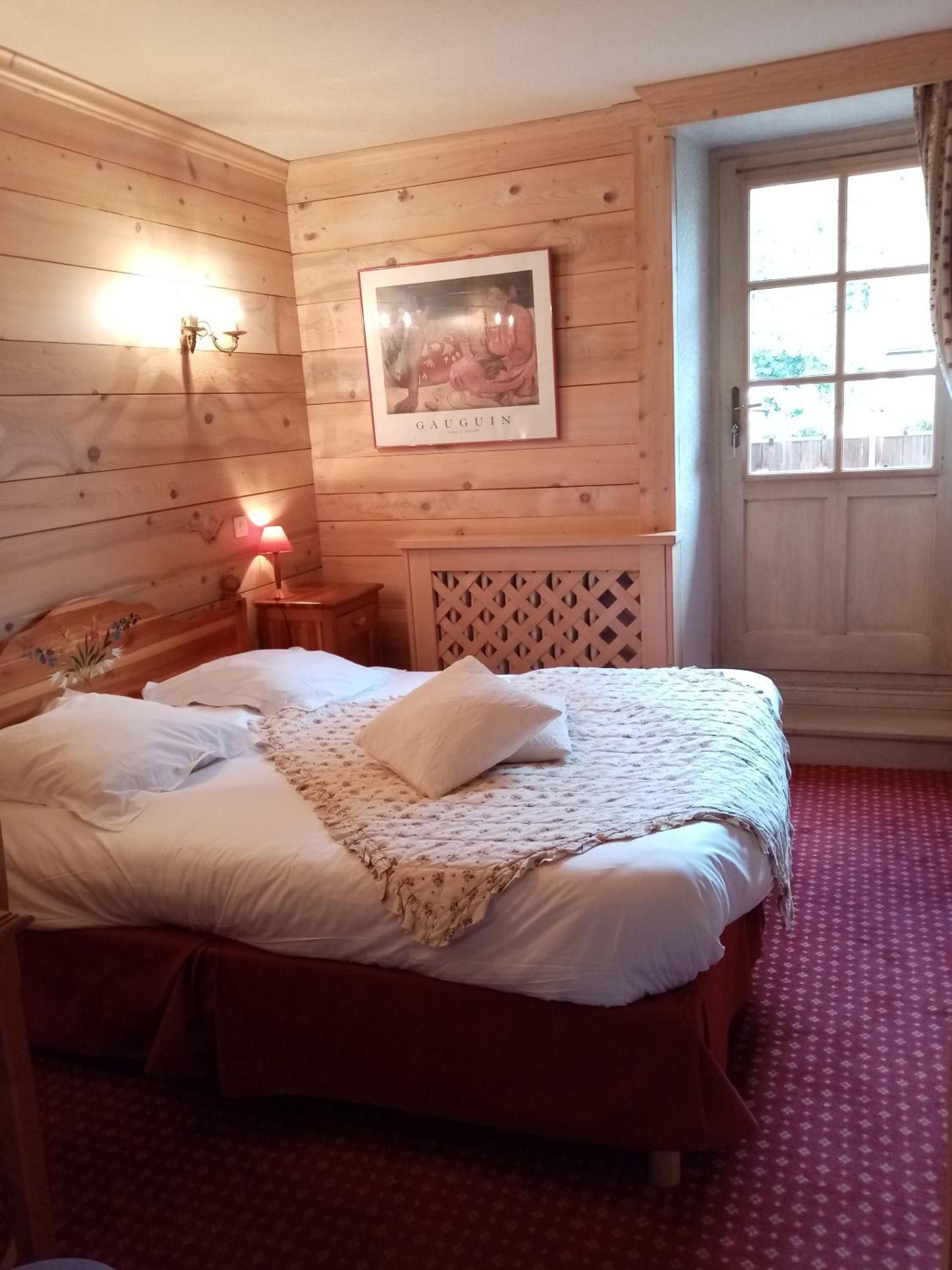 A wooden-paneled room with a bed, a framed picture, a nightstand, and a window with curtains.