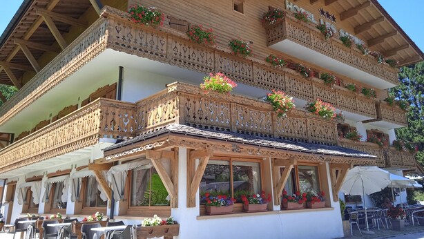 Un edificio de madera tradicional con balcones decorados con flores, mesas al aire libre y un letrero que indica que es un hotel.