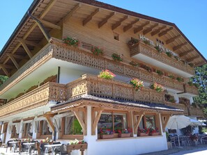 Un bâtiment traditionnel en bois, doté de balcons ornés de fleurs, d’une terrasse et d’une enseigne indiquant qu’il s’agit d’un hôtel.