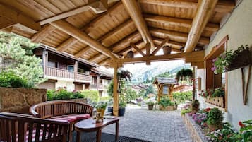 Une terrasse couverte en bois, aménagée avec du mobilier d’extérieur, des plantes en pot et offrant une vue sur un village de montagne.