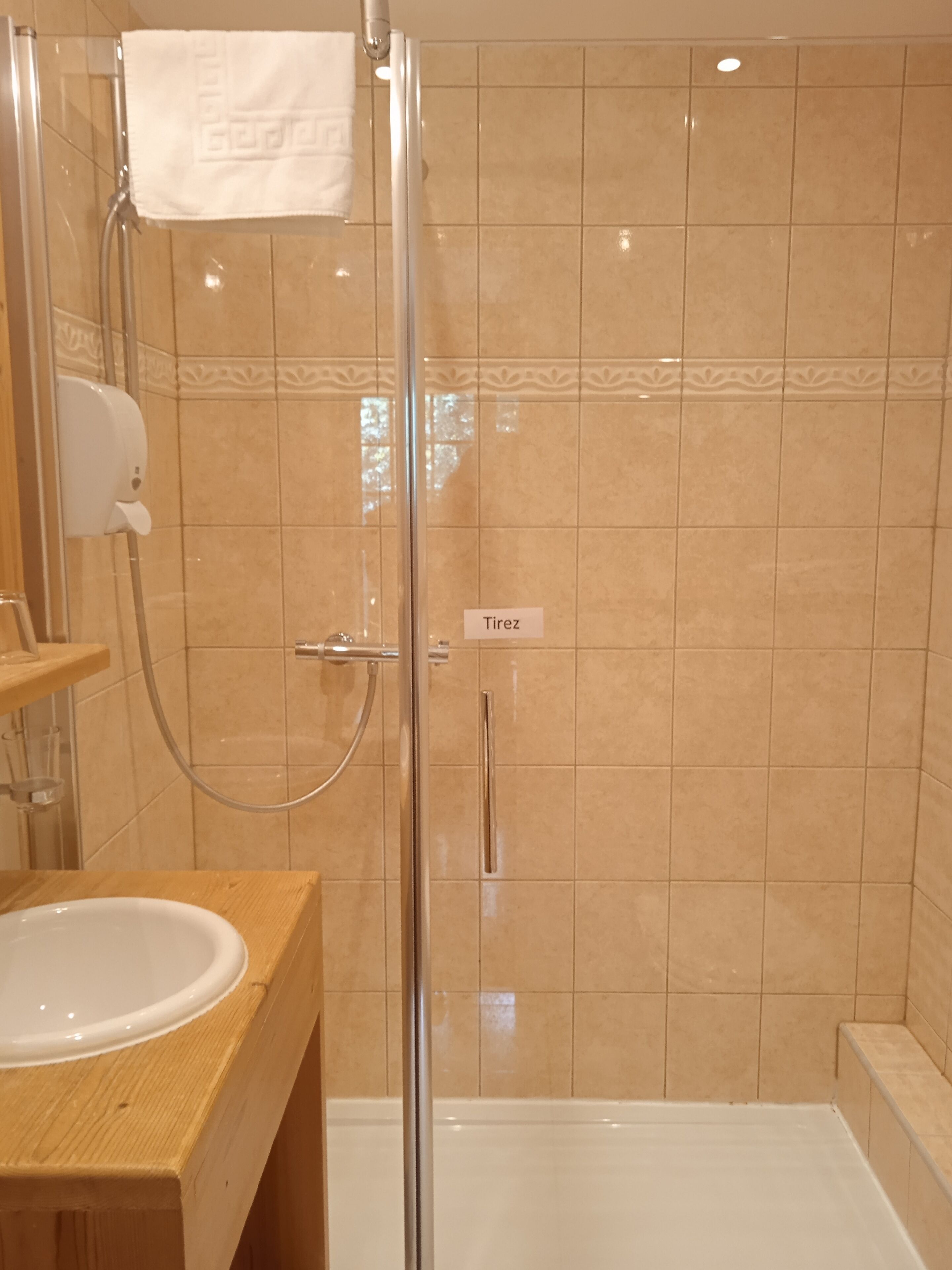 A bathroom with a glass-enclosed shower, a wooden vanity with a sink, and beige tiled walls.