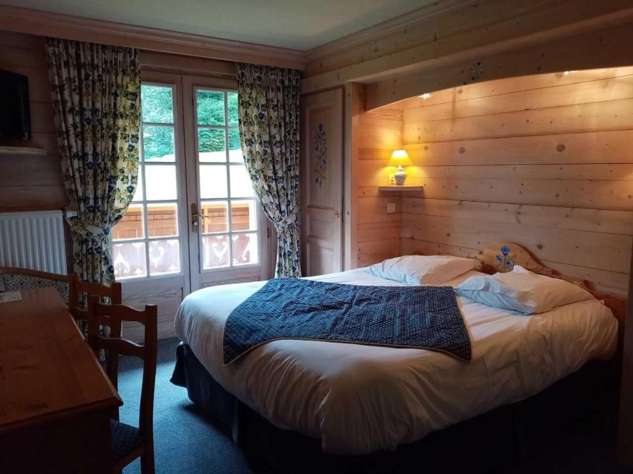 Quarto com cama, mesa de cabeceira com abajur, janela com cortinas e parede de madeira.