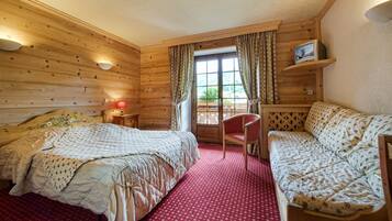 A wooden cabin bedroom with two beds, a red carpet, a TV on a shelf, and a window with curtains.