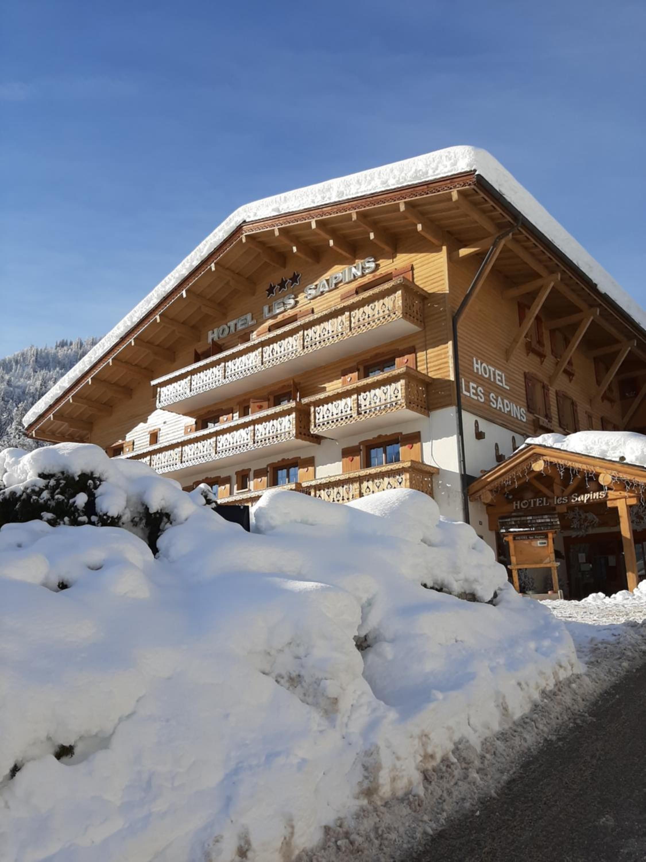 Un hotel con fachada de madera, varios balcones y alrededores cubiertos de nieve.