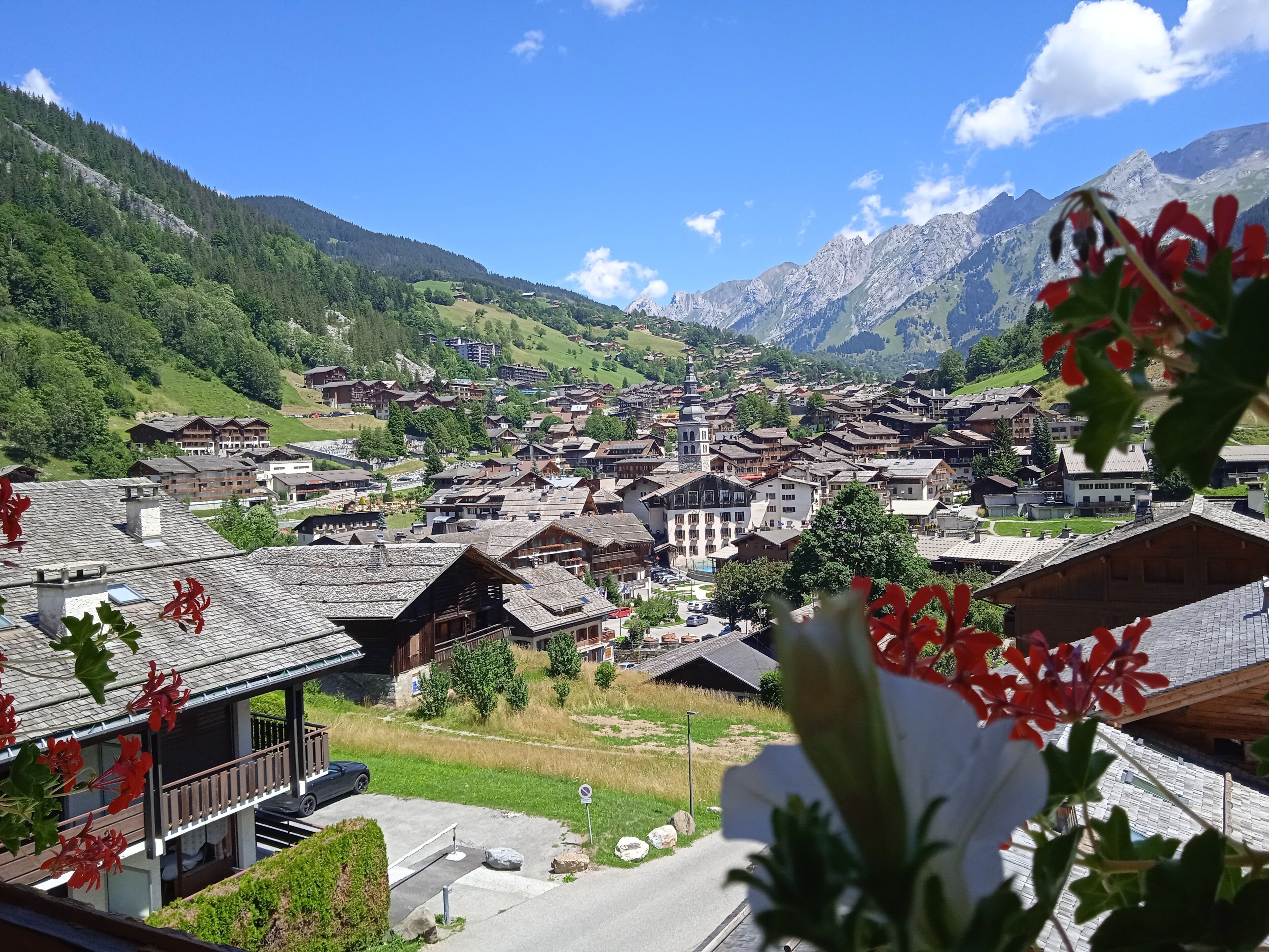 Un village de montagne aux maisons traditionnelles en bois, avec une église centrale et une vue sur des montagnes enneigées.