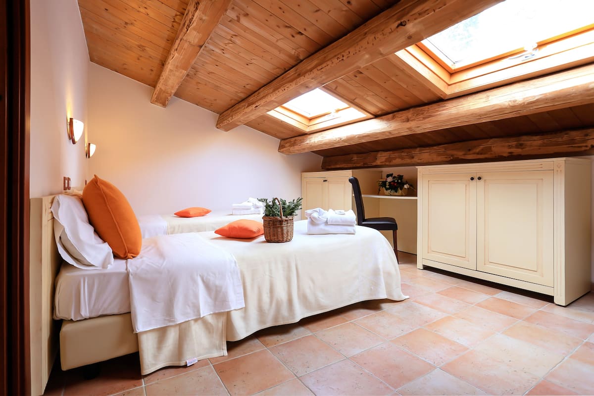 A bedroom with two beds, a skylight, wooden beams, a chair, and a cabinet.