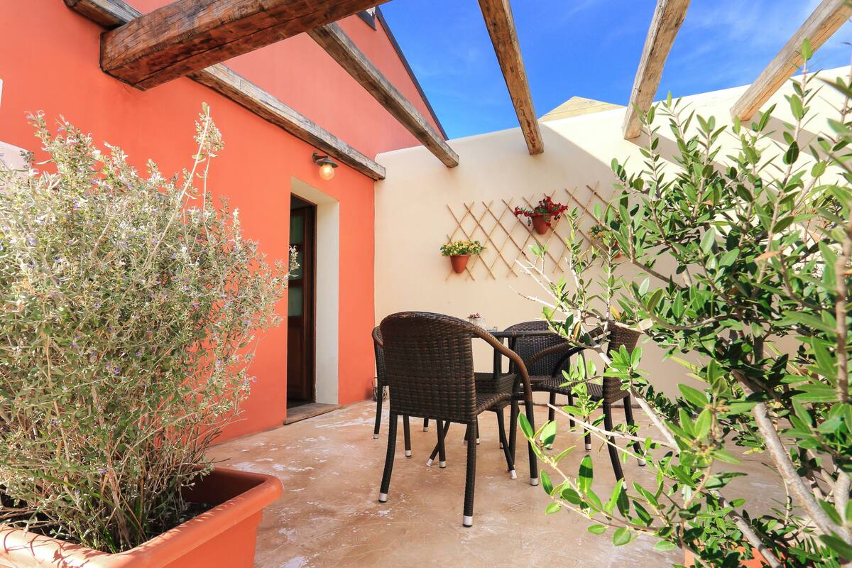 An outdoor patio with wicker furniture, potted plants, and a wooden pergola structure.