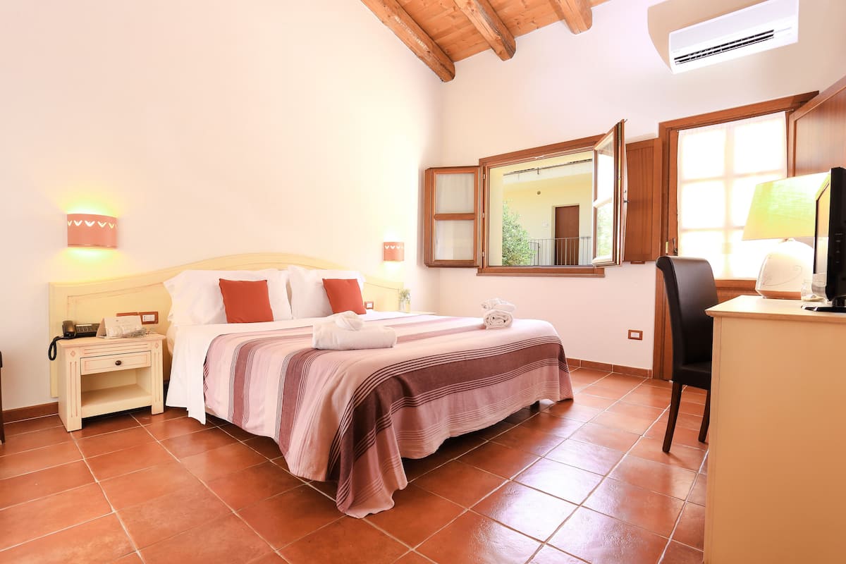 A bedroom with a bed, bedside table, lamp, and a desk with a chair.