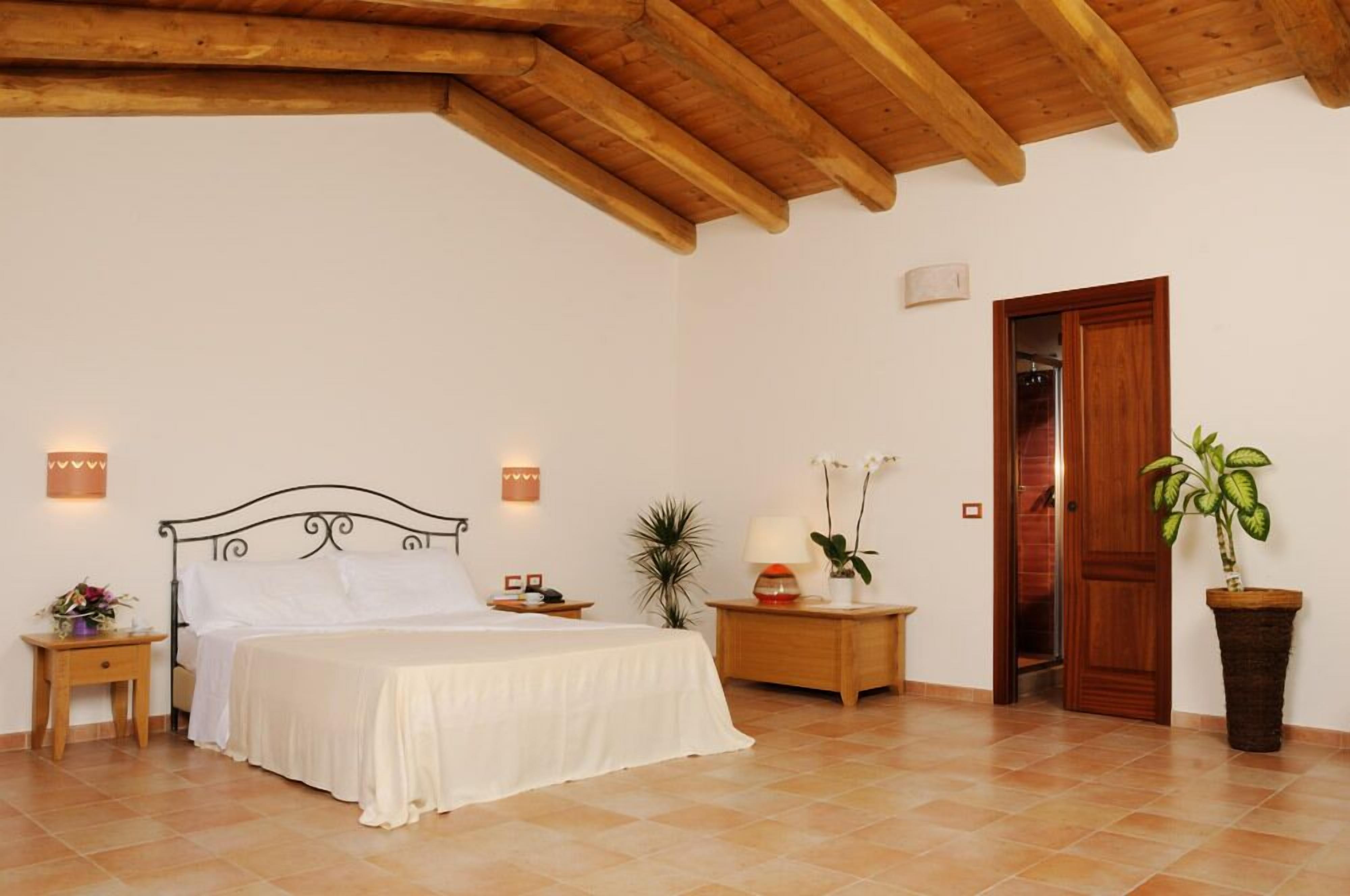 A bedroom with a bed, bedside tables, a nightstand, a potted plant, and a wooden door.