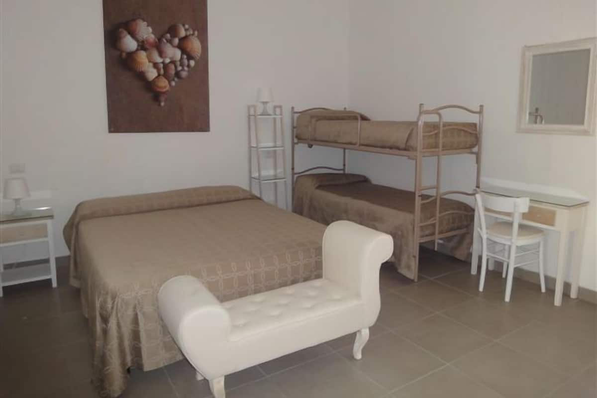 Um quarto com beliches, escrivaninha, cadeira, mesa de cabeceira e prateleira fixada na parede.