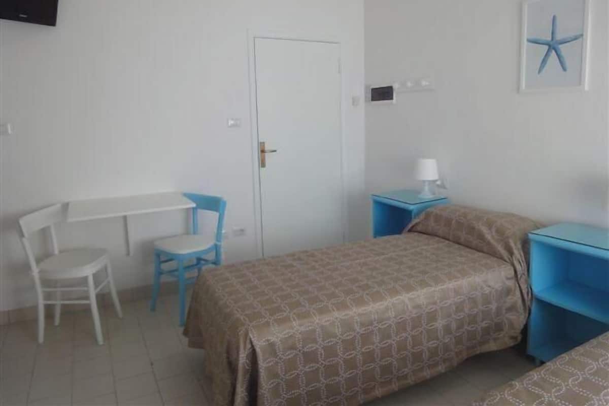 Quarto com cama, escrivaninha, cadeira e televisão na parede.