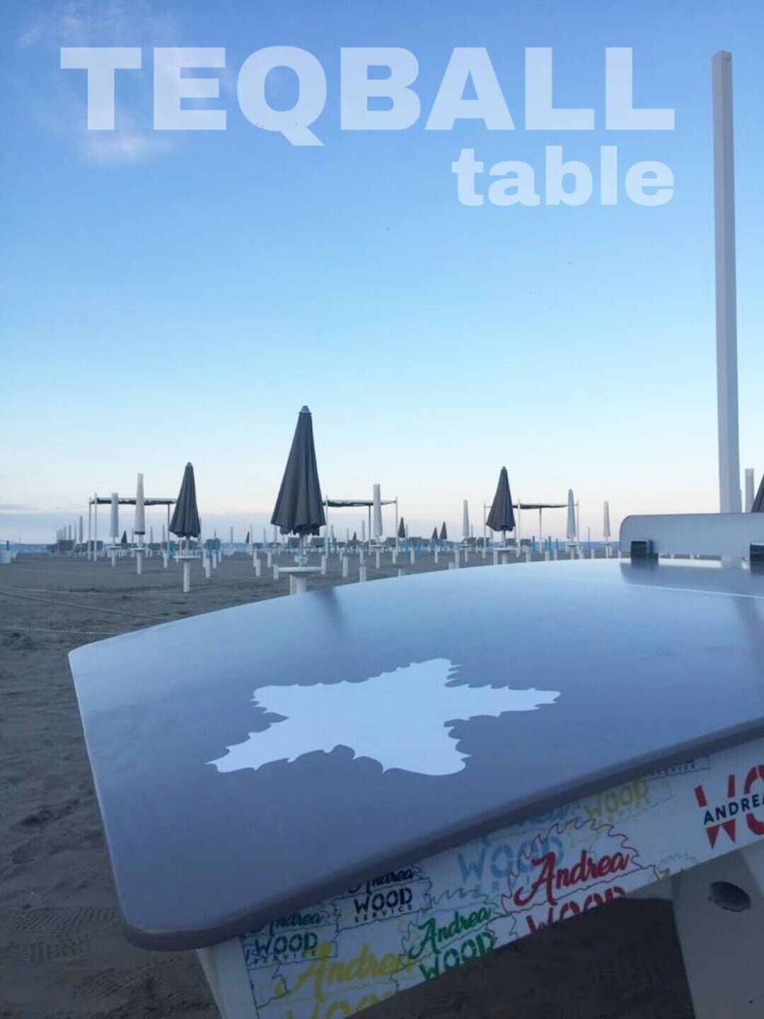 Et bord ved stranden med et kortmønster, omgivet af parasoller og strandstole mod en klar himmel.