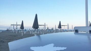 Et bord ved stranden med et kortmønster, omgivet af parasoller og strandstole mod en klar himmel.