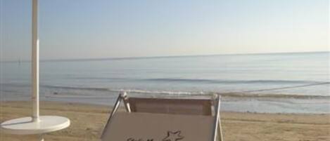 A beach chair with a logo, an umbrella, and a white table.
