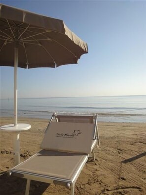 A beach chair with a logo, an umbrella, and a white table. - Ostello Casa per Ferie Stella Marina - Hostel (Cesenatico)