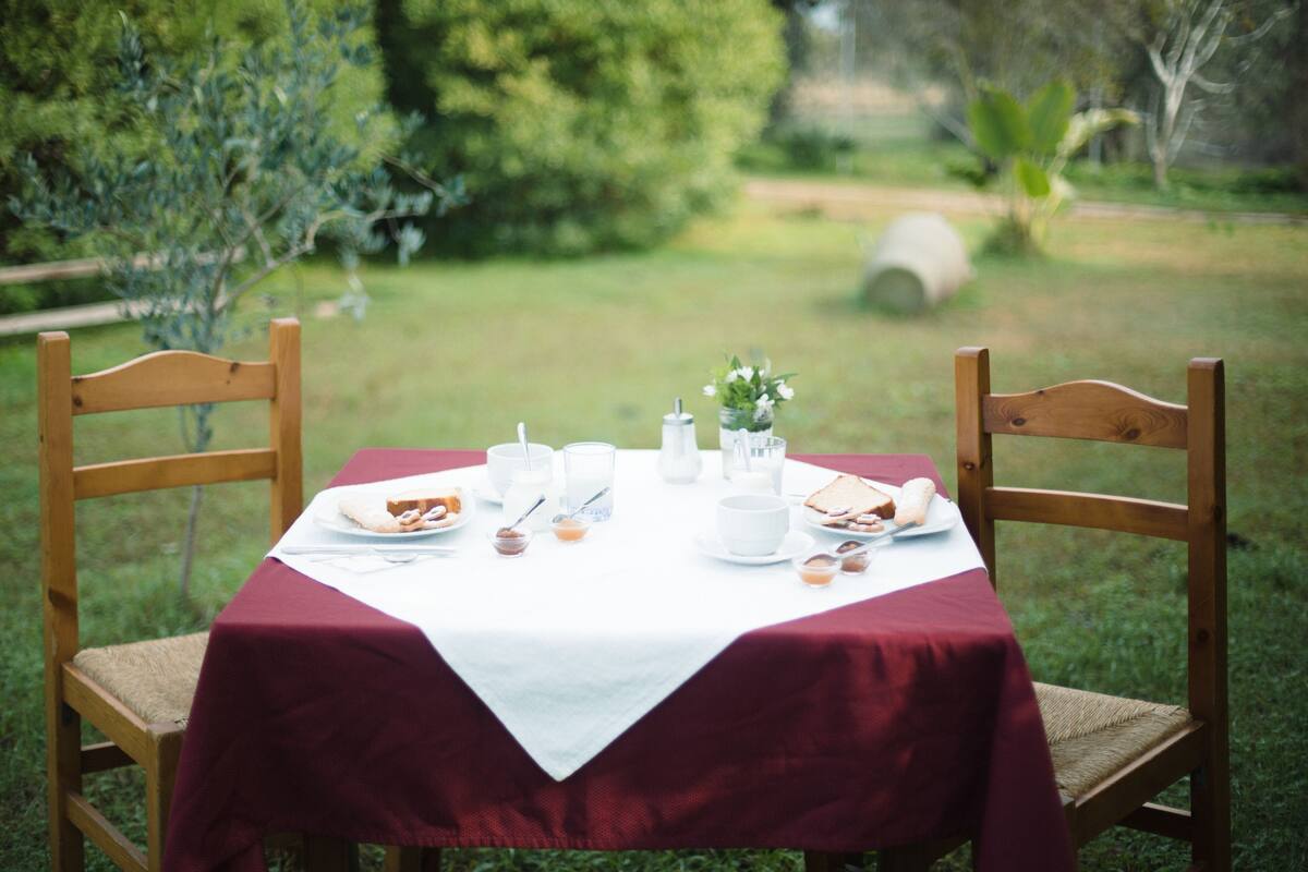 A table set outdoors with a white tablecloth and wooden chairs.