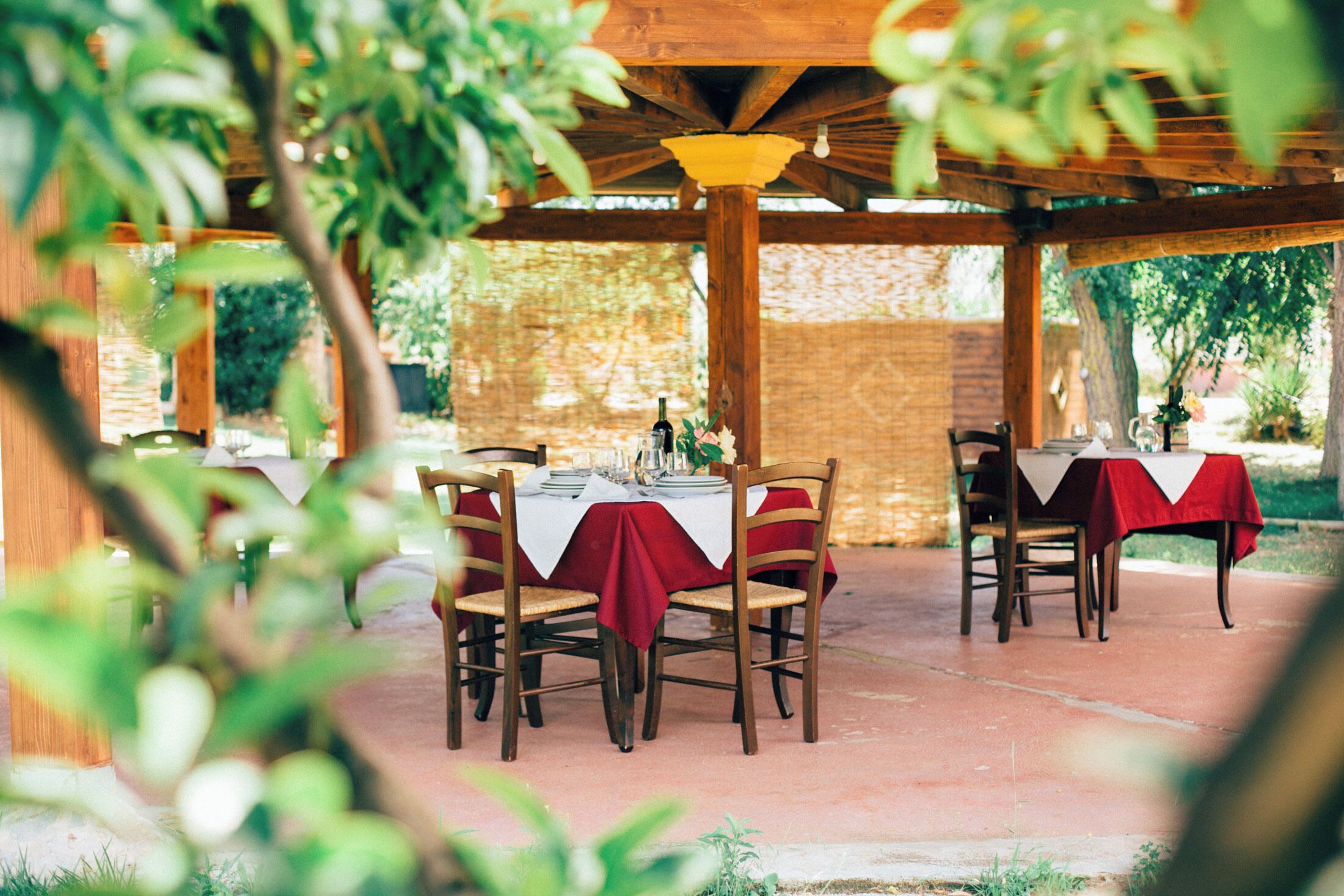 Un patio al aire libre con mesas y sillas de madera, cubierto por una pérgola de madera.