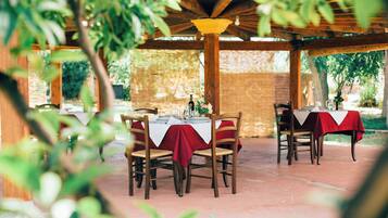 Un patio al aire libre con mesas y sillas de madera, cubierto por una pérgola de madera.