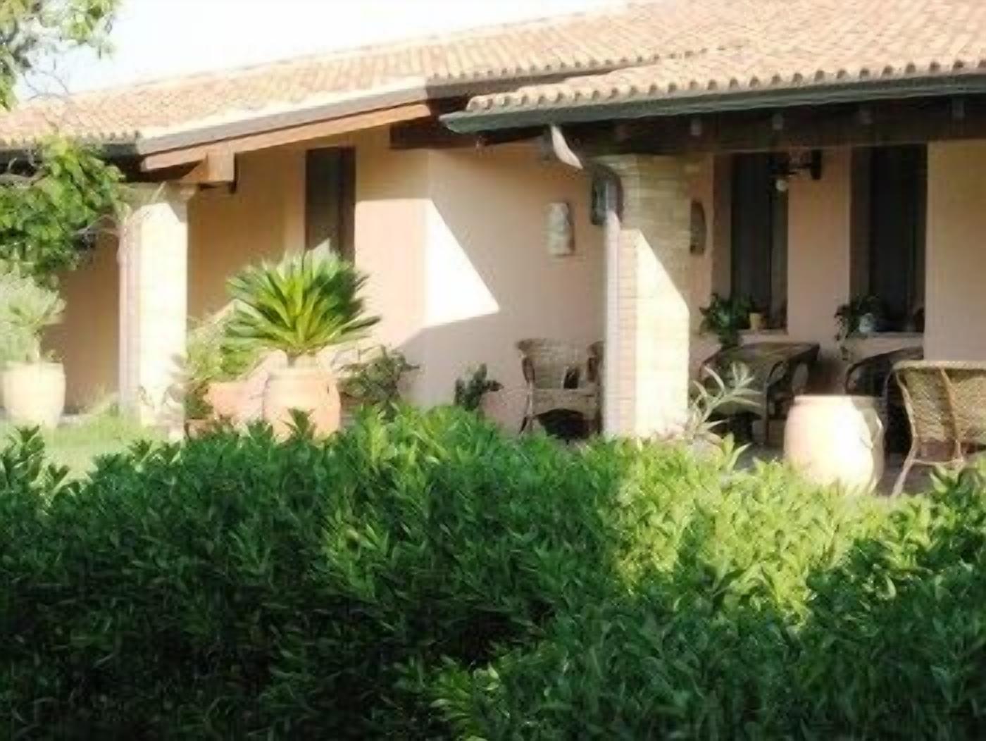 Uma casa com telhado de cerâmica, varanda coberta com cadeiras e plantas em vasos.