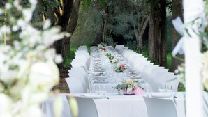 An outdoor dining area with white tablecloths and chairs, set against a backdrop of trees and greenery. - Su Leunaxiu (Soleminis)