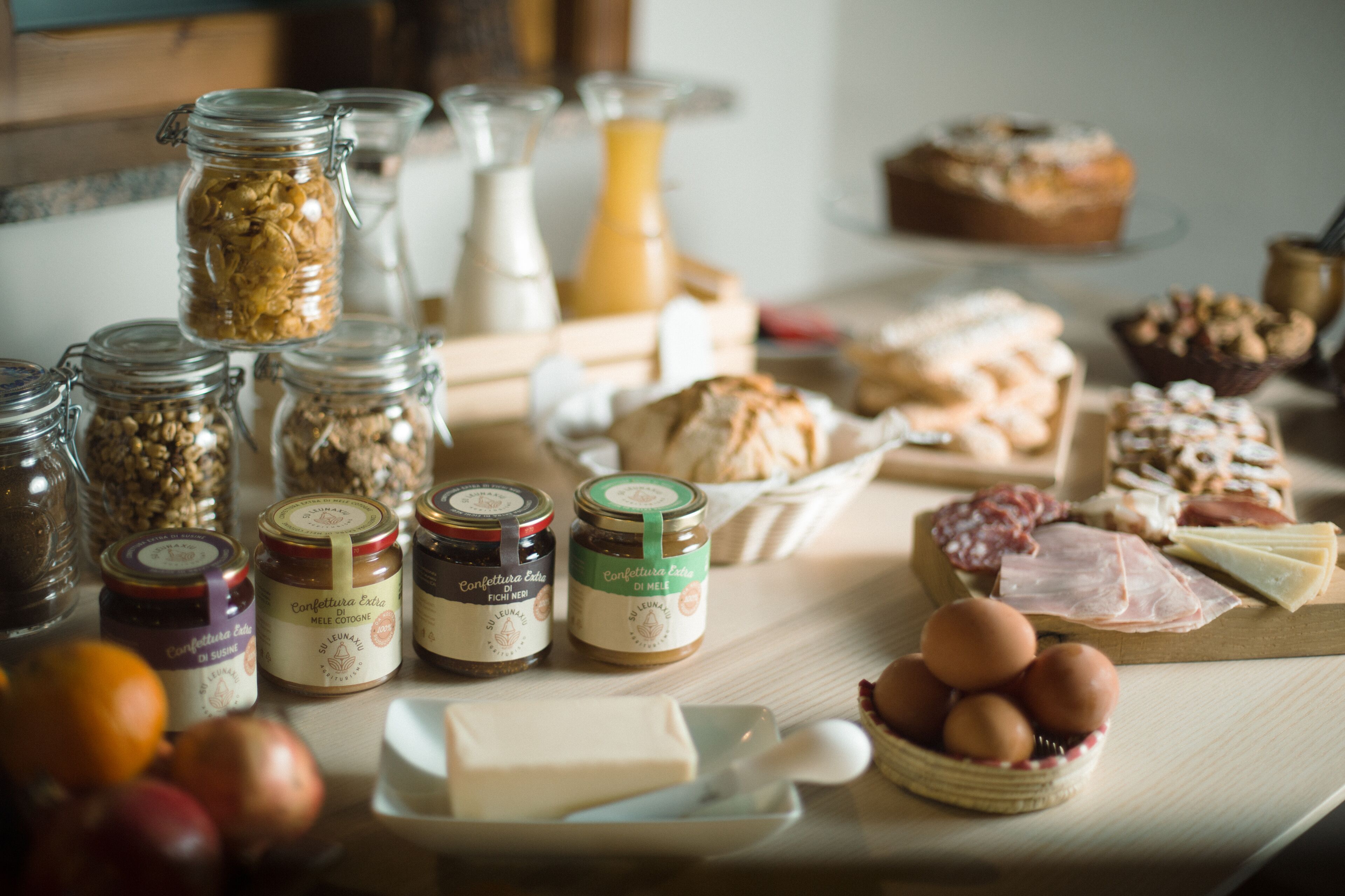 A variety of food items including jars of preserves, cheese, and meats on a wooden table.