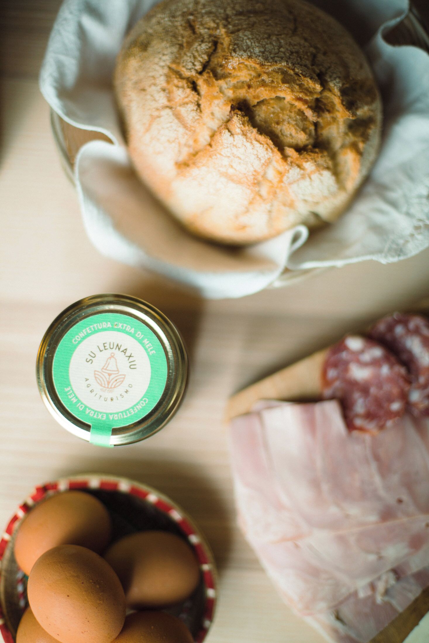 A loaf of bread, a jar of honey, eggs, and a piece of meat on a wooden surface.