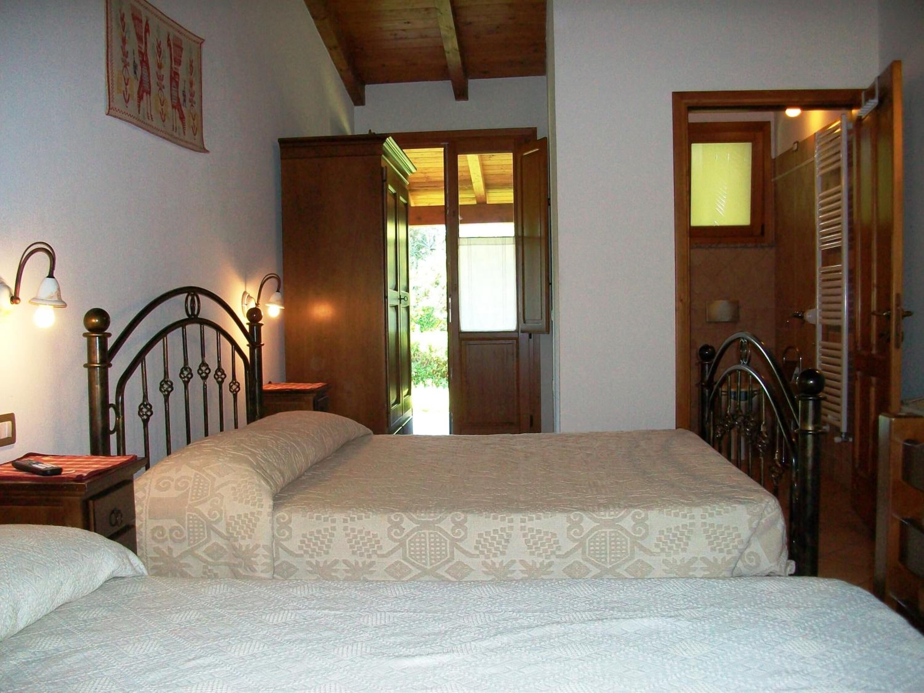A bedroom with two beds, wooden headboards, a nightstand, a wall-mounted lamp, and a door leading to a balcony.