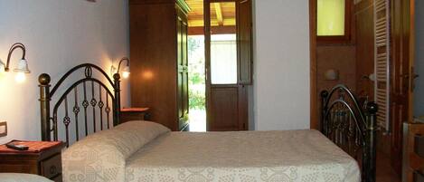 A bedroom with two beds, wooden headboards, a nightstand, a wall-mounted lamp, and a door leading to a balcony.