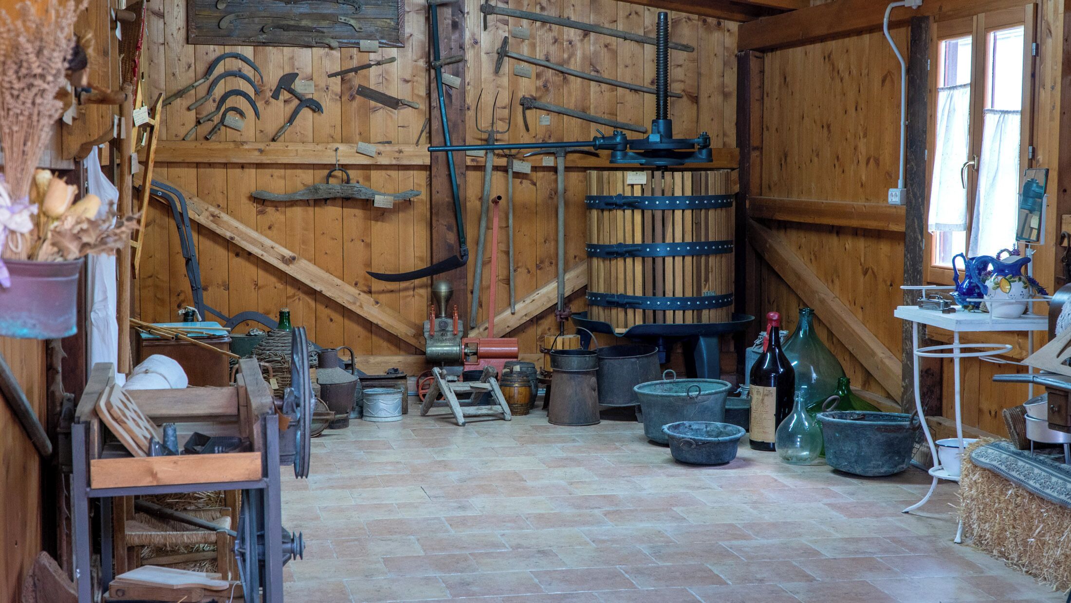 Una habitación rústica de madera con diversas herramientas, barriles y una pequeña mesa con jarras y botellas.