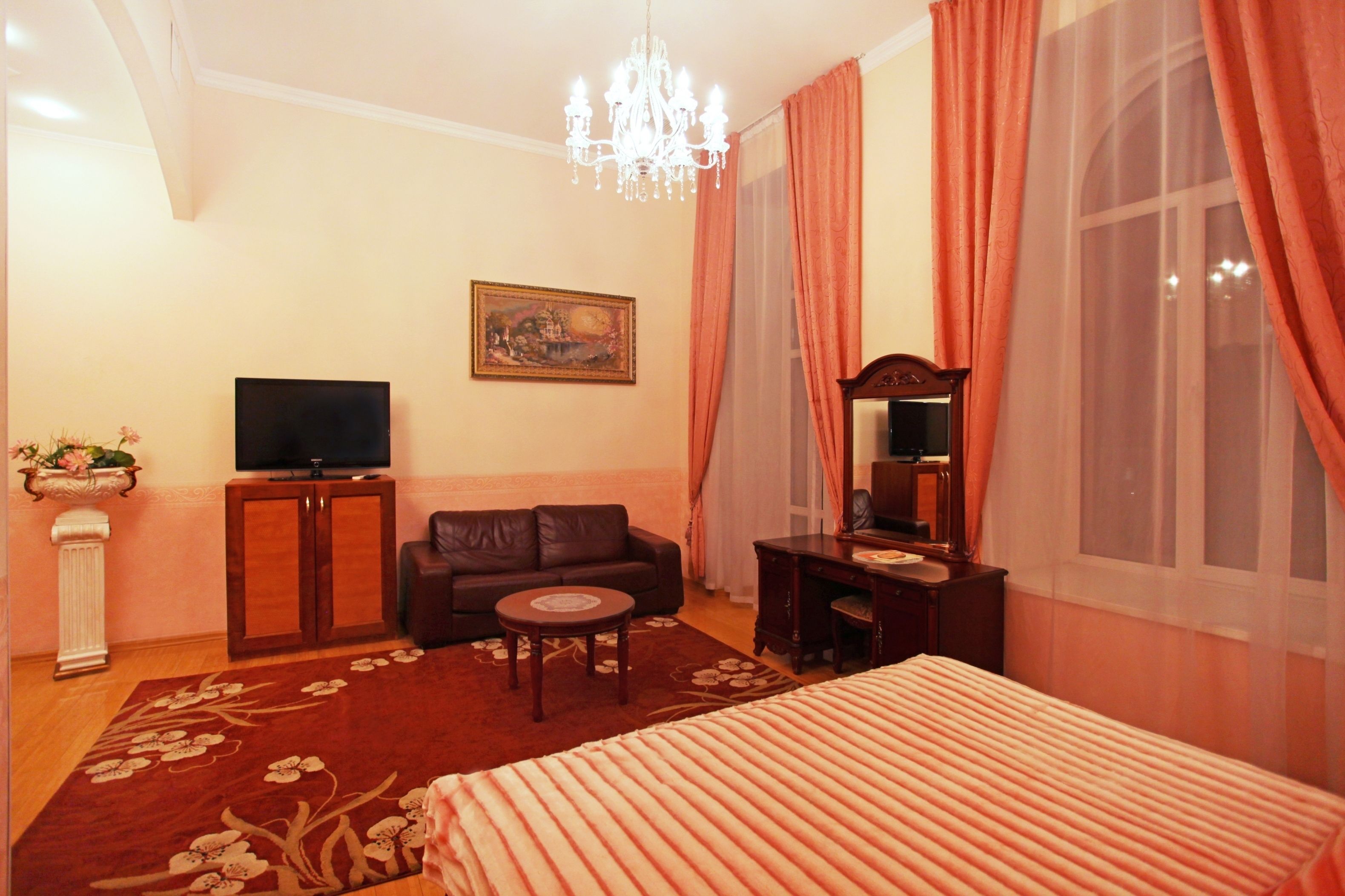 A hotel room with a bed, a sofa, a TV, a desk, and a chandelier.