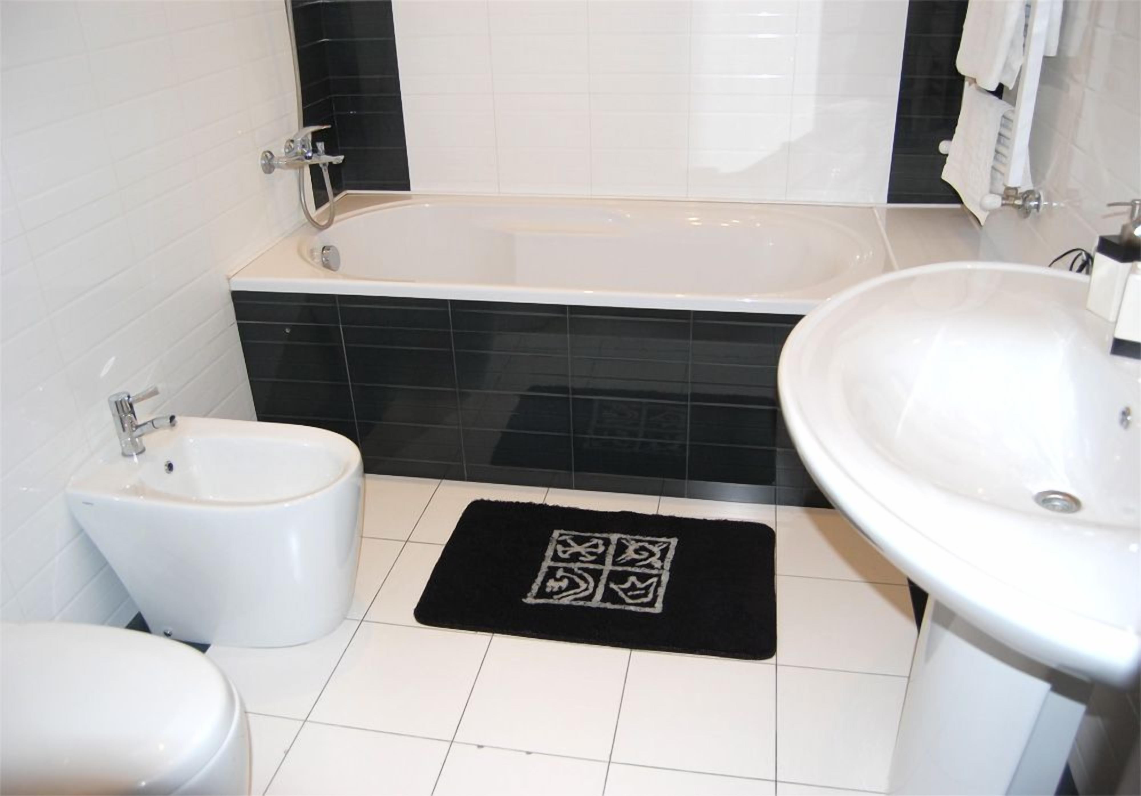 Un baño con bañera, bidé, lavabo y una alfombra negra.