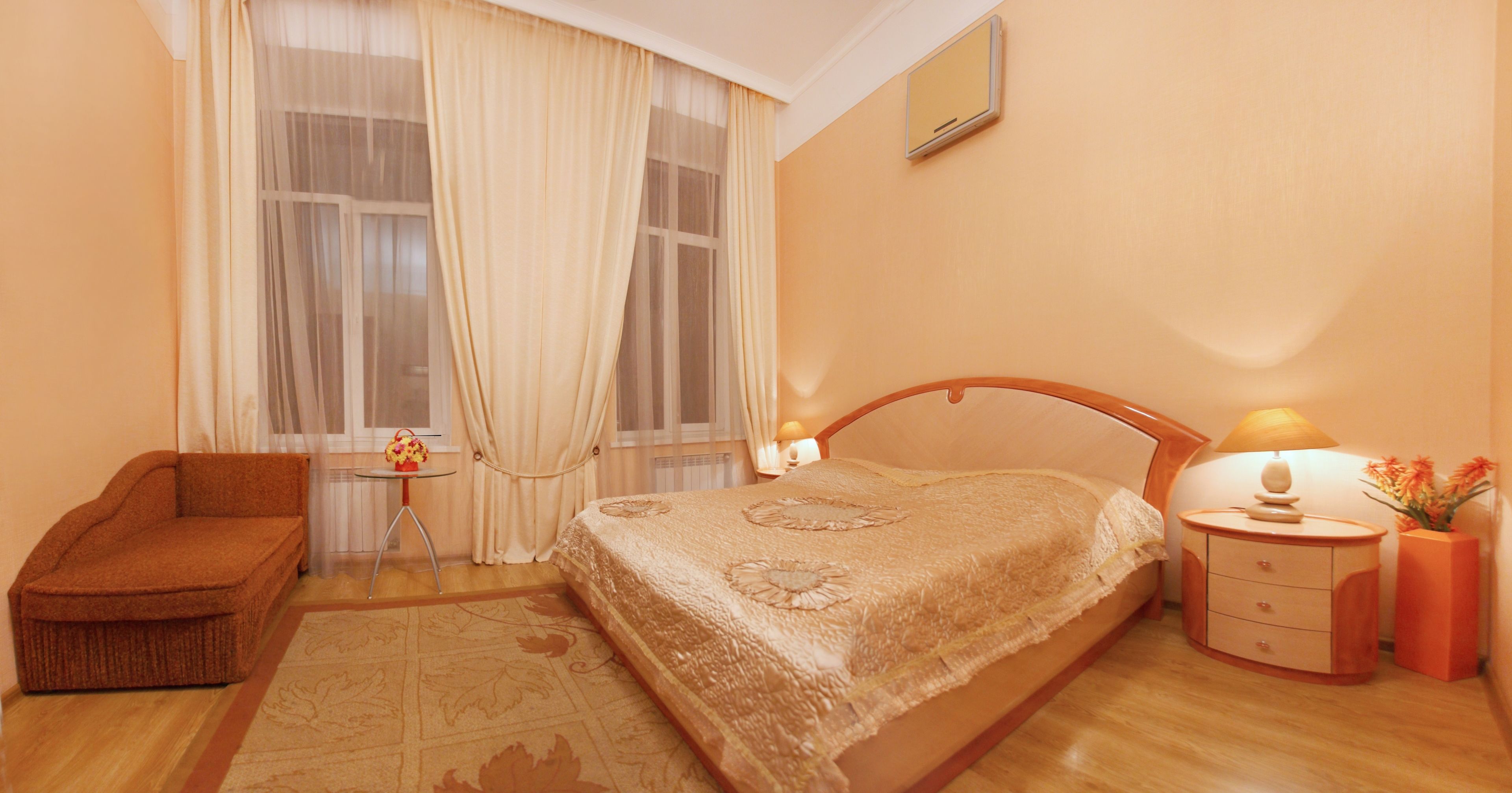 A bedroom with a bed, a nightstand, a chair, a small table, and a window with curtains.