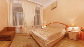 A bedroom with a bed, a nightstand, a chair, a small table, and a window with curtains.