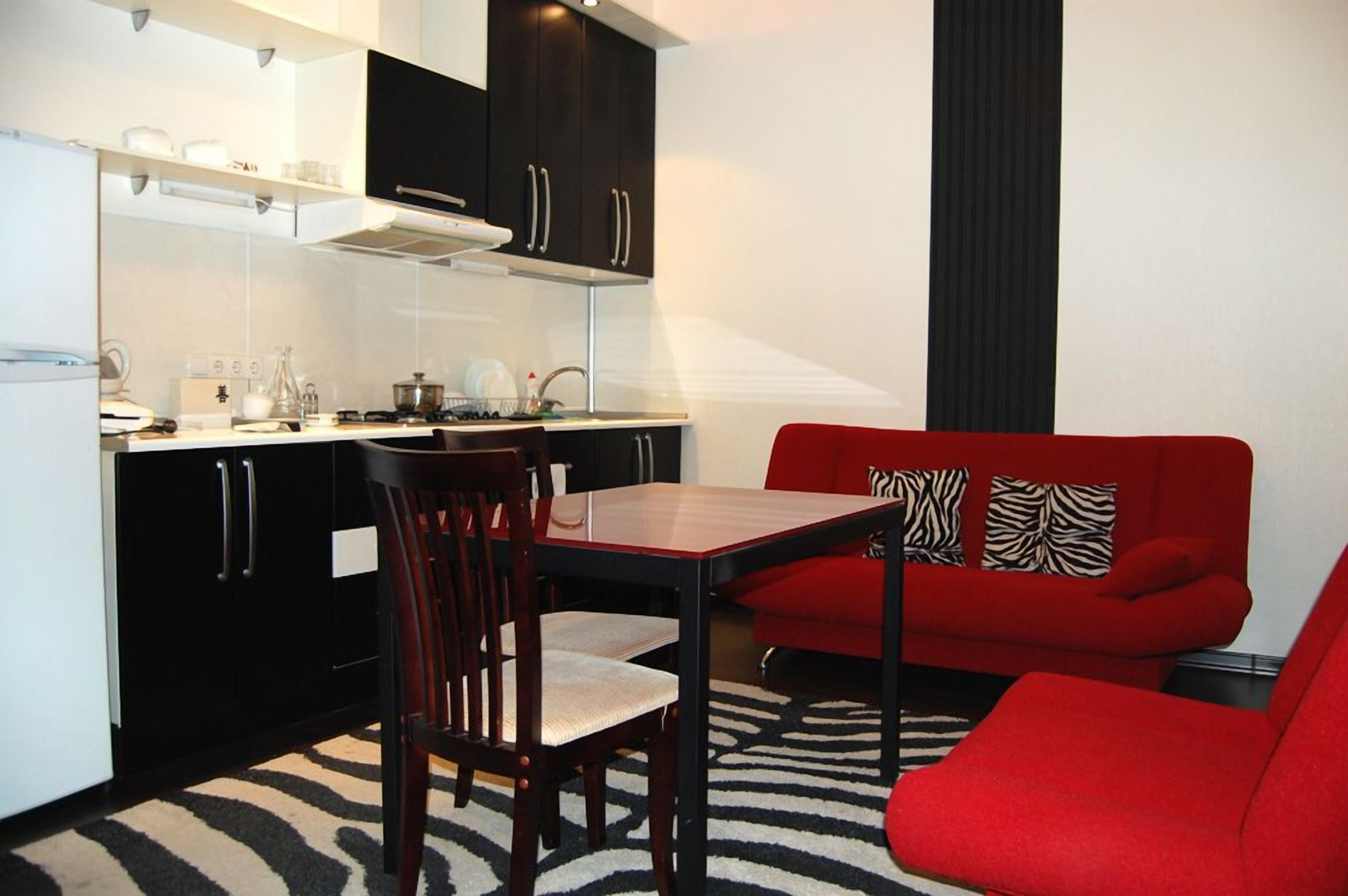 A compact kitchen with a dining area, featuring a red sofa and a zebra-patterned rug.