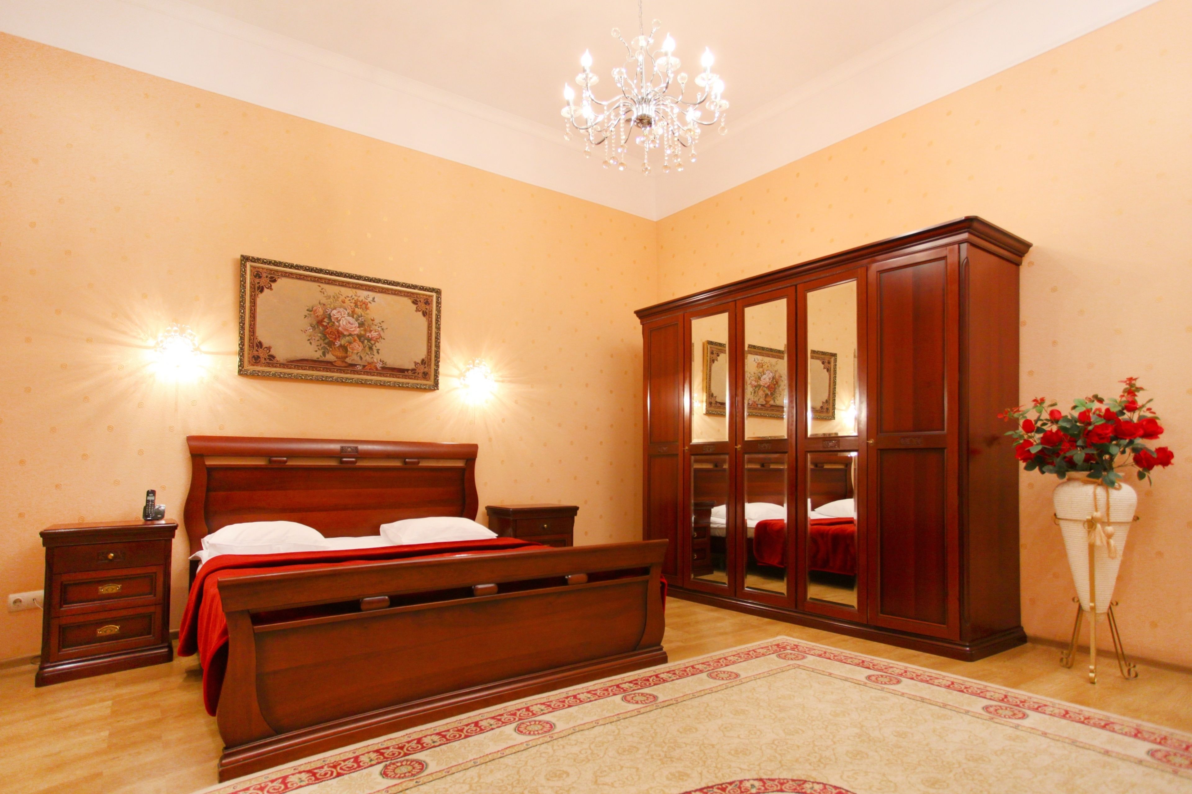 Un dormitorio con una cama de madera, una mesita de noche, un armario, una araña y un espejo en la pared.