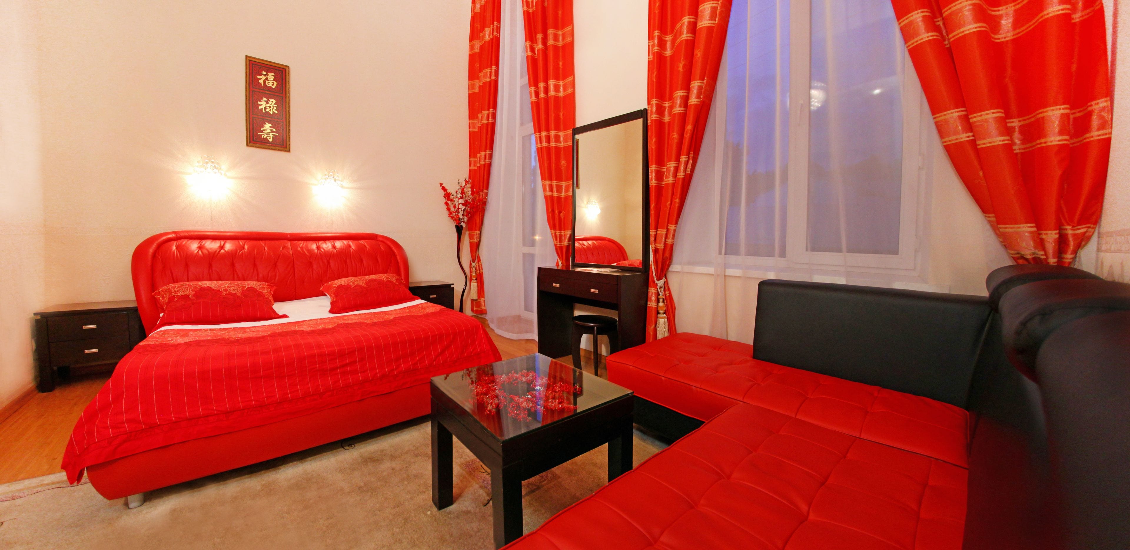 A bedroom with a red bed, a black sofa, a glass coffee table, and a mirror.